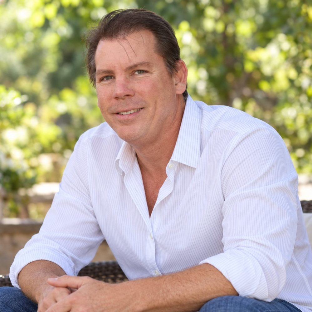 John Kirker, seated outdoors in a white shirt